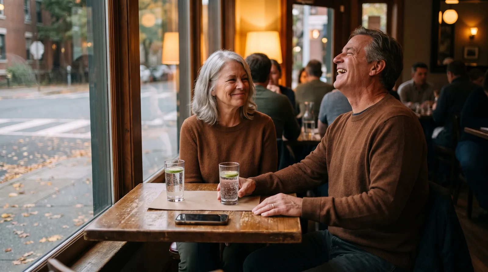 A husband and wife sharing a relaxed dinner at a neighborhood restaurant, his phone face down at the edge of the table